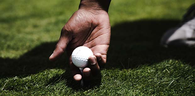 Man Holding Golf ball on a tee in the grass